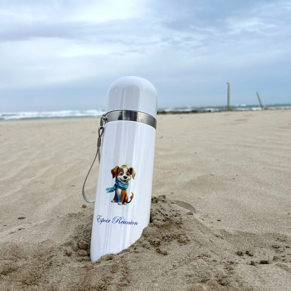 thermos blanc planté dans le sable, il y a une illustration d'un chien marron qui porte une écharpe