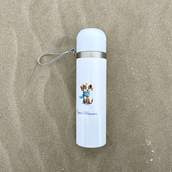 thermos blanc avec une illustration de chien marron posé sur le sable. Le thermos comporte une dragonne en tissus gris